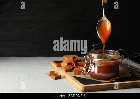 Vaso di vetro con caramello salato e caramelle su sfondo grigio, spazio per il testo Foto Stock