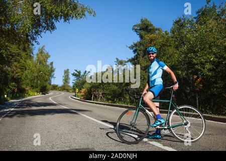 Un uomo con una bici di montagna. Serpentina di strada di montagna, circondata da una foresta. Il Kazakistan, Almaty, Medeo Foto Stock