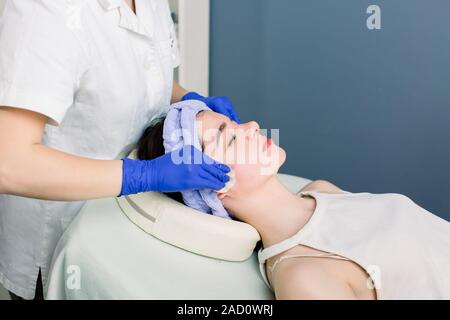 Mani femminili di estetista deterge la pelle con tamponi di cotone. Cura della pelle del viso. La donna caucasica su una procedura di cosmetologia. Visita al salone di bellezza Foto Stock