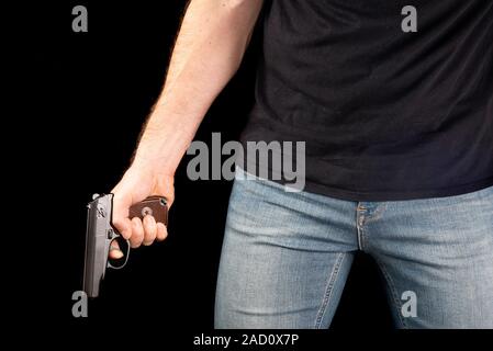 Un uomo con una pistola in mano su uno sfondo nero. Killer con una pistola Foto Stock