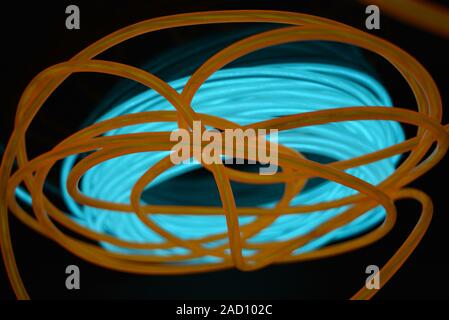 Una bobina di luminosi di turchese, cielo blu filo luminoso con fili  caotica di una luce arancione guida situata su un nero la superficie lucida  Foto stock - Alamy