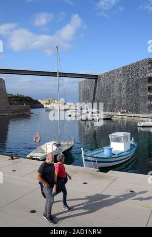 Coppia di turisti Middle-Aged camminando lungo la banchina del porto con barche da pesca nella parte anteriore del museo MUCEM Marsiglia Provenza Francia Foto Stock
