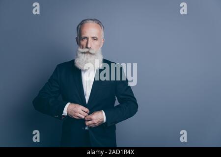 Ritratto di sua egli bella attraente chic elegante grigio gravi dai capelli uomo macho, dandy indossando tux pulsante di fissaggio isolate su grigio scuro a colori pastello Foto Stock