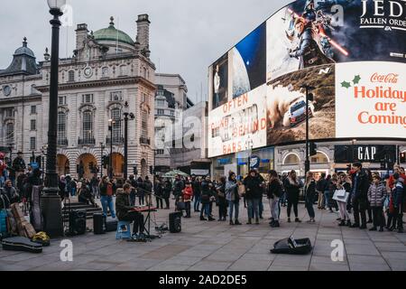 London, Regno Unito - 24 Novembre 2019: folla suonatore ambulante guardare la riproduzione di tastiera e cantando su Piccadilly Circus, una delle zone turistiche più popolari in Lond Foto Stock