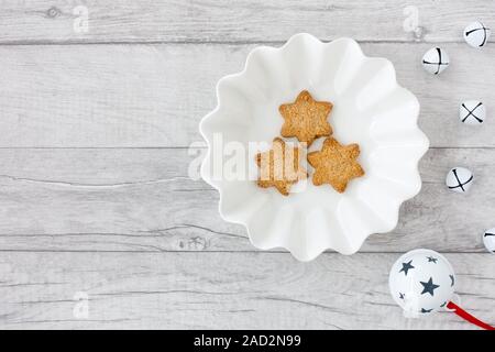 A forma di stella biscotti di Natale in bianco ciotola con Jingle Bells su legno bianco sullo sfondo del pannello con copia spazio. Vista dall'alto. Foto Stock