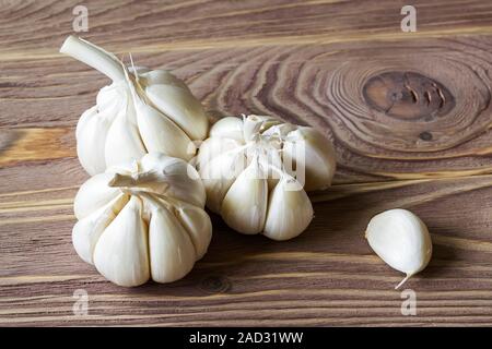 Tre teste di aglio crudo e uno spicchio su un marrone tavolo in legno. Piccante ingrediente di cottura. Vitamina cibo sano. Verdure e piatti vegetariani. Vista dall'alto. Foto Stock