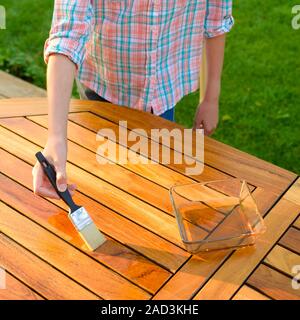 Mano che tiene un pennello applicare vernice vernice su una tavola di legno Tavolo da giardino Foto Stock