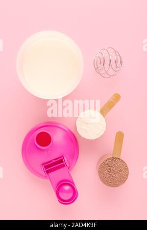 Proteine in polvere con un agitatore e latte fresco su sfondo rosa Foto Stock