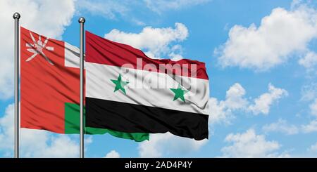 Oman e Siria bandiera sventolare nel vento contro bianco torbido cielo blu insieme. Concetto di Diplomazia e relazioni internazionali. Foto Stock
