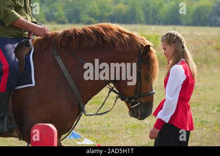 Samara, Russia - 07 Ottobre 2019: giovani e cosacco cosacco ragazza in costumi nazionali in piedi accanto al cavallo. La ragazza dice addio al Cossac Foto Stock