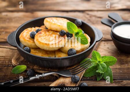 Delizioso cottage cheese frittelle o syrniki con mirtilli freschi in ghisa padella in legno scuro dello sfondo rustico. Deliziosa pausa Foto Stock