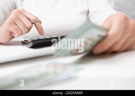 Risparmi, finanze, economia e home concetto - close up delle mani con la calcolatrice conteggiare denaro e rendere note a casa Foto Stock