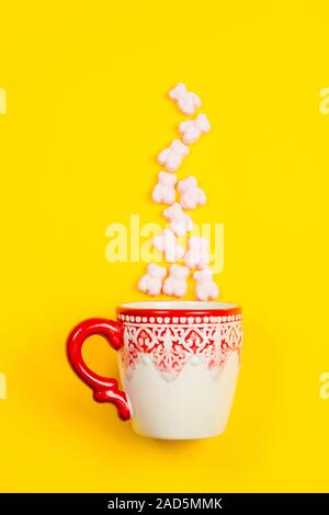 Marshmallows, cubetti di zucchero candito e bastoni in una vacanza mug su sfondo giallo Foto Stock
