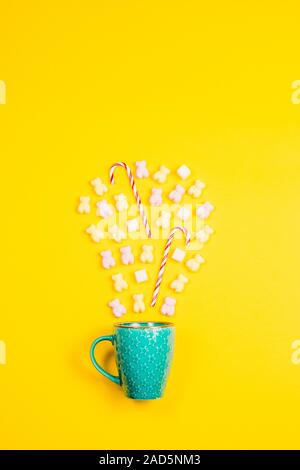 Marshmallows, cubetti di zucchero candito e bastoni in un turchese star mug su sfondo giallo Foto Stock