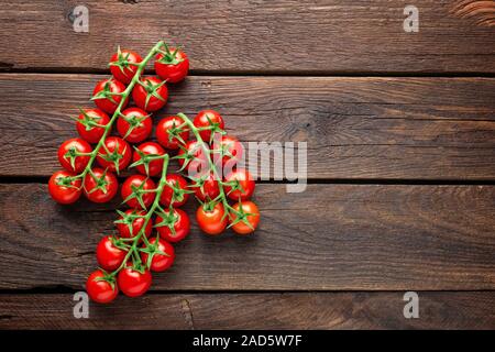 Freschi pomodori ciliegia su ramoscelli sul tavolo di legno, vista dall'alto Foto Stock