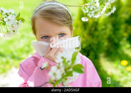 Allergia. Bambina soffia il naso vicino alla molla albero in fiore - starnuti ragazza. Bambino con un fazzoletto Foto Stock