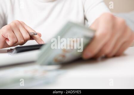 Risparmi, finanze, economia e home concetto - close up delle mani con la calcolatrice conteggiare denaro e rendere note a casa Foto Stock