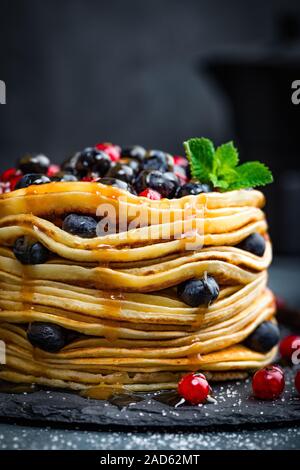 Frittelle con frutti di bosco freschi e sciroppo d'acero su sfondo scuro, primo piano Foto Stock