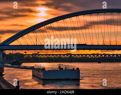 Il ponte Apollo attraversa il Danubio al tramonto a Bratislava, in Slovacchia, con cielo arancione e riflessi. Foto Stock