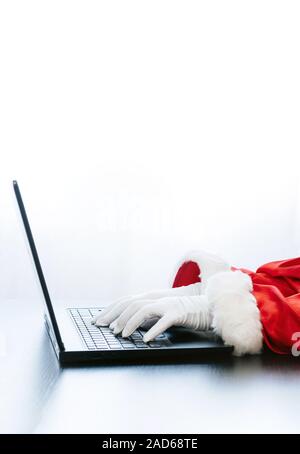 Babbo Natale utilizzando portatile su sfondo bianco. Vestito in guanti bianchi mani di Santa digitando dal computer. Foto Stock