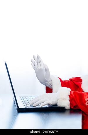 Babbo Natale utilizzando portatile su sfondo bianco. Vestito in guanti bianchi mani di Santa digitando dal computer. Foto Stock