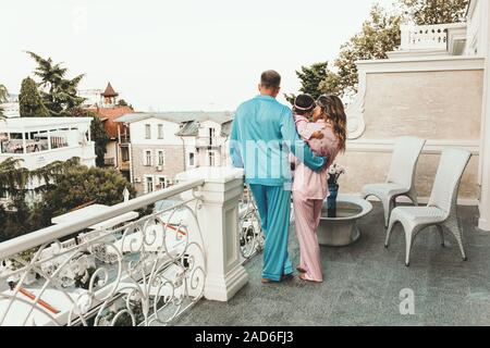 Bella famiglia sul balcone dell'hotel gode della vista sulla città, in nightgowns colazione in hotel, felice giovani genitori con un bambino Foto Stock