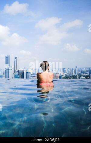 Femmina guardando sopra la skyline di Singapore nella piscina a sfioro di Marina Bay Sands Foto Stock