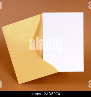 Busta in oro con un messaggio vuoto card o invito isolata su uno sfondo di colore marrone. Spazio per la copia. Foto Stock
