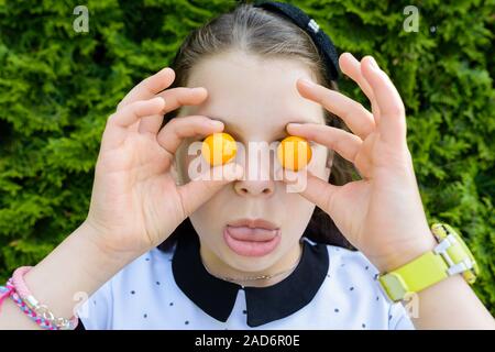 Ritratto di giovane, sorridendo felice girl holding, mostra piccoli pomodori oltre i suoi occhi, ridendo Foto Stock