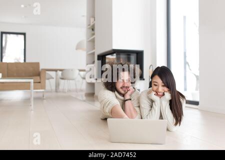 Giovane coppia multietnica utilizzando un computer portatile sul pavimento Foto Stock