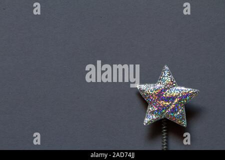 Close-up silver glitter star in plastica con molla su uno sfondo grigio, concetto minimalista o dello sfondo Foto Stock