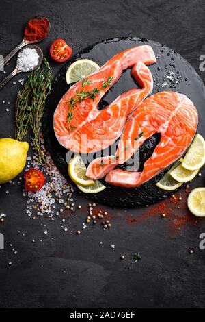 Crudo fresco salmone pesce rosso bistecche su sfondo nero. Vista superiore Foto Stock