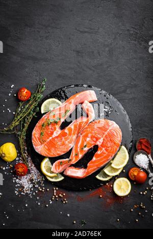 Crudo fresco salmone pesce rosso bistecche su sfondo nero. Vista superiore Foto Stock