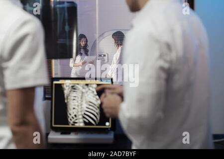 Nella sala di controllo medico radiologo e discutere della diagnosi mentre si guarda la procedura, in Background subisce paziente MRI o CT Procedura di scansione. Foto Stock