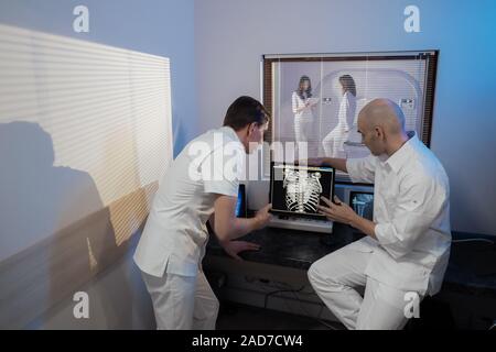 Nella sala di controllo medico radiologo e discutere della diagnosi mentre si guarda la procedura, in Background subisce paziente MRI o CT Procedura di scansione. Foto Stock