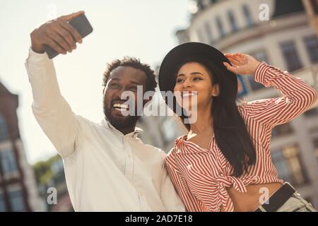Signora sorridente toccando il suo orlo di cappello mentre prendere foto con il mio ragazzo Foto Stock