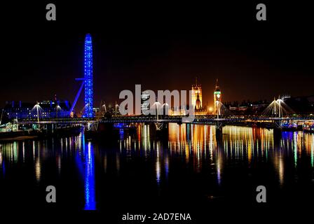Un tempo di notte vista di Hungerford Bridge da Waterloo Bridge con il London Eye e Westminster all'orizzonte e riflessa nel fiume Tamigi. Foto Stock