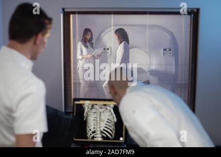 Nella sala di controllo medico radiologo e discutere della diagnosi mentre si guarda la procedura, in Background subisce paziente MRI o CT Procedura di scansione. Foto Stock