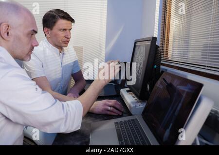 Nella sala di controllo medico radiologo e discutere della diagnosi mentre si guarda la procedura, in Background subisce paziente MRI o CT Procedura di scansione. Foto Stock