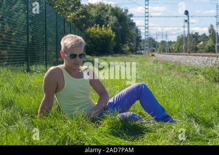 Giovane uomo in giallo t-shirt seduto sull'erba e guardare su di voi Foto Stock