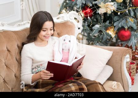 Club di letteratura. Lo spirito di natale. Lettore poco godetevi la lettura a casa. Capodanno. Bambina la lettura di storia di Natale. Miglior libro di Natale. Negozio di libri commerciali. Poco sorridente bambino leggere il libro. Foto Stock