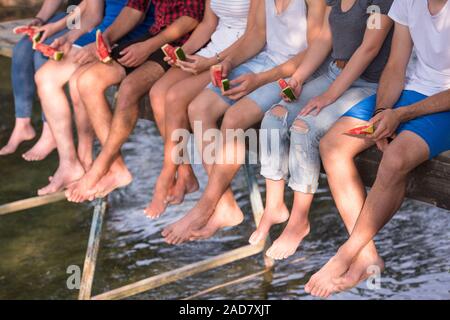 Amici godendo di cocomero mentre è seduto sul ponte di legno Foto Stock