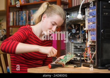 Ragazza con un cacciavite su una scheda di espansione scheda di circuito stampato a partire da un PC aperto mentre si eseguono interventi di riparazione del computer. Foto Stock