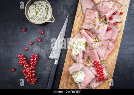 Pranzo Tradizionale di carne con affettati misti arrosto di manzo decorate con salsa remoulade e ribes rosso in alto su un taglio di bo Foto Stock