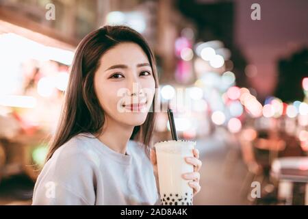 Donna asiatica gustare latte bolla tè con cibo di strada nella notte di mercato Foto Stock