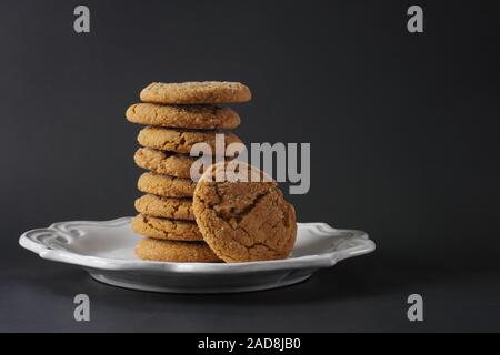 Una pila di fragranti biscotti allo zenzero su una piastra bianca e uno sfondo nero; spazio di copia Foto Stock