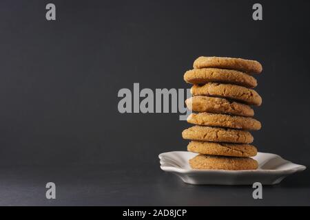 Una pila di gingerbread cookie su una piastra bianca con uno sfondo nero; spazio di copia Foto Stock