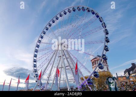 Vista ad angolo basso della ruota panoramica bianca gigante un cielo blu gainst sulle bancarelle decorate di Weihnachtsmarkt, mercatino di Natale, a Burgplatz in Düsseldorf. Foto Stock