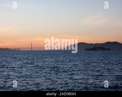 San Francisco skyline della città, il Golden Gate Bridge e Isola di Alcatraz al tramonto, visto dall'Isola del Tesoro, con le onde di laminazione e nuvole drammatico in Cali Foto Stock