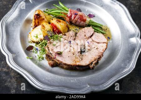 Barbecue greco marinato arrosto di agnello con patate e fagioli laminati in pancetta come primo piano su una piastra in peltro Foto Stock